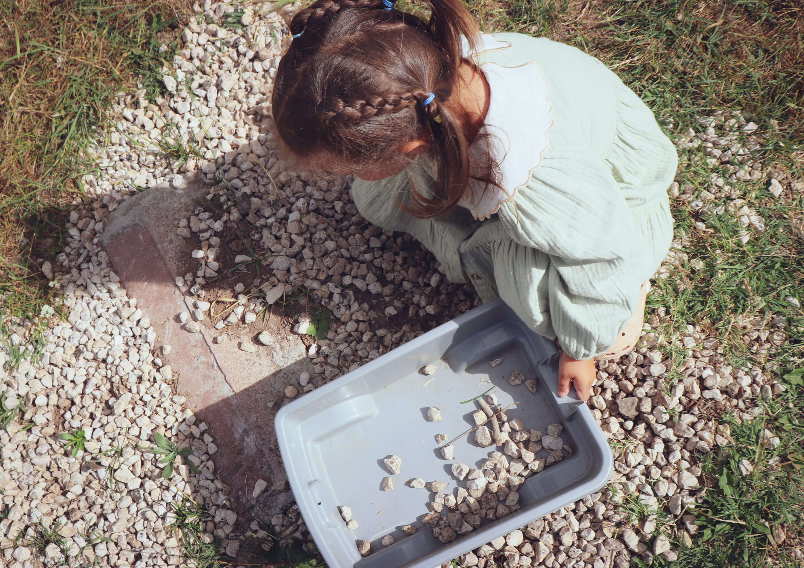 A child crouching on a gravel path, sorting stones into a tray