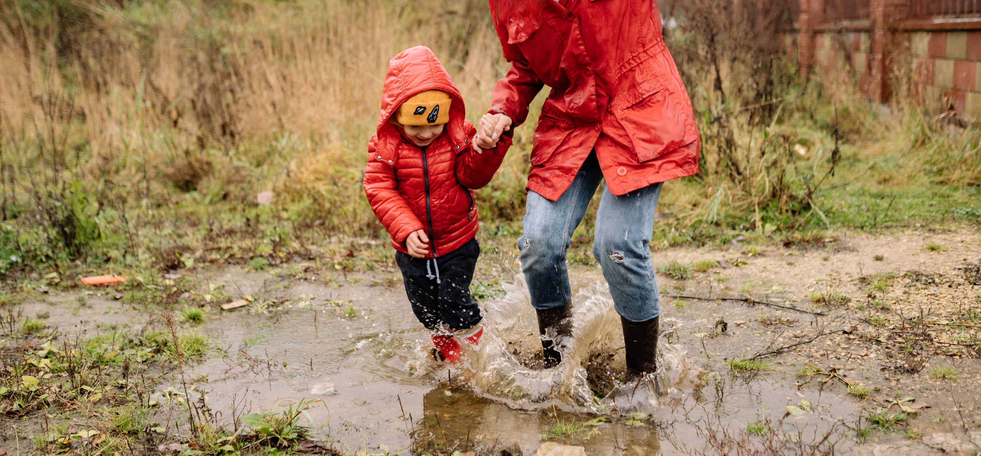 An adult and a child in raincoats splashing through a puddle together